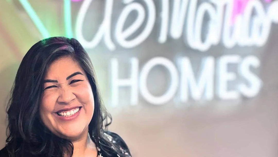 Flor De Maria McNally smiling in front of the deMaria Homes sign