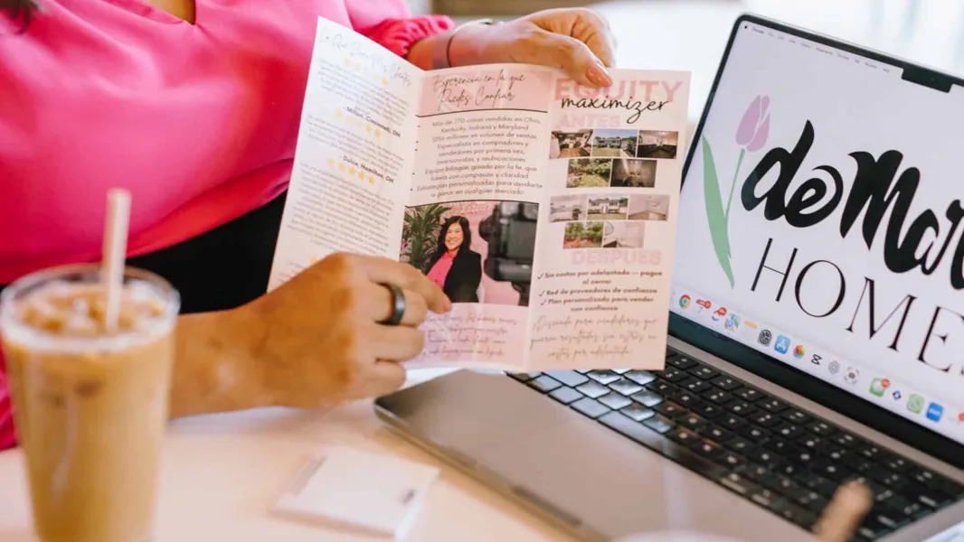 Reviewing printed client materials beside a laptop showing the deMaria Homes logo