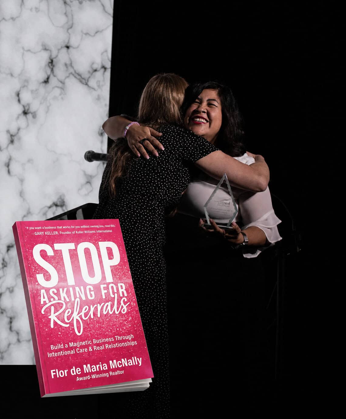 Flor embracing a friend, with her book Stop Asking for Referrals