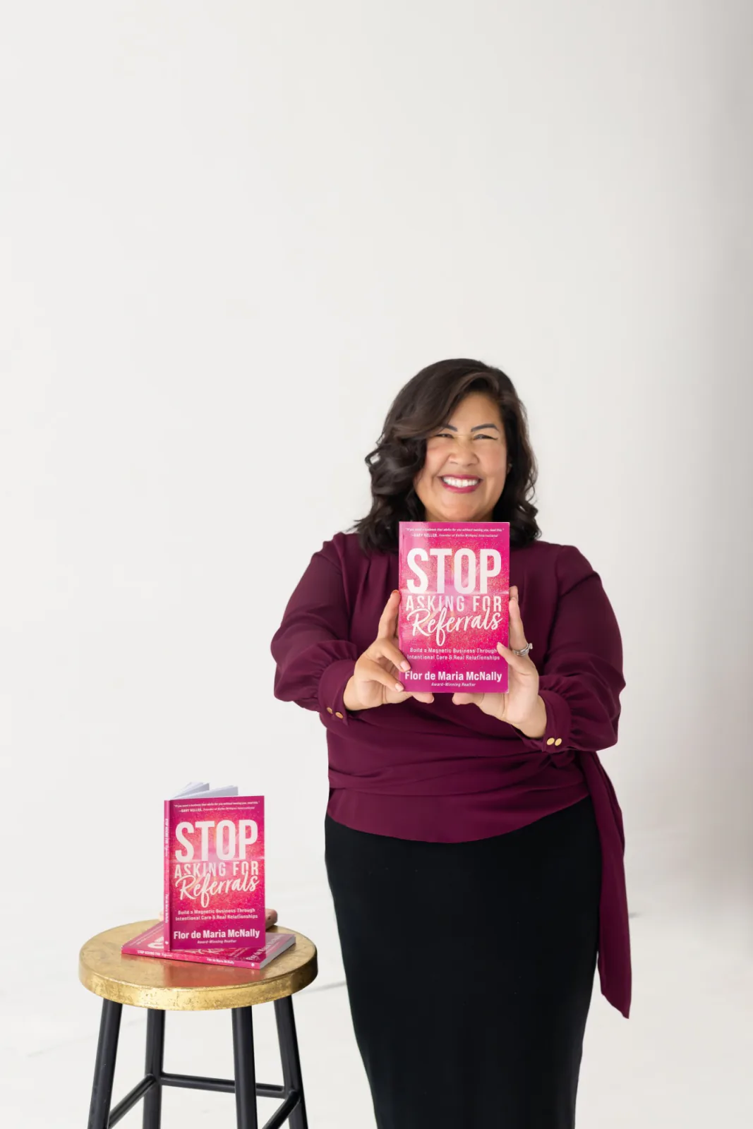Flor De Maria McNally smiling and holding out her book Stop Asking for Referrals